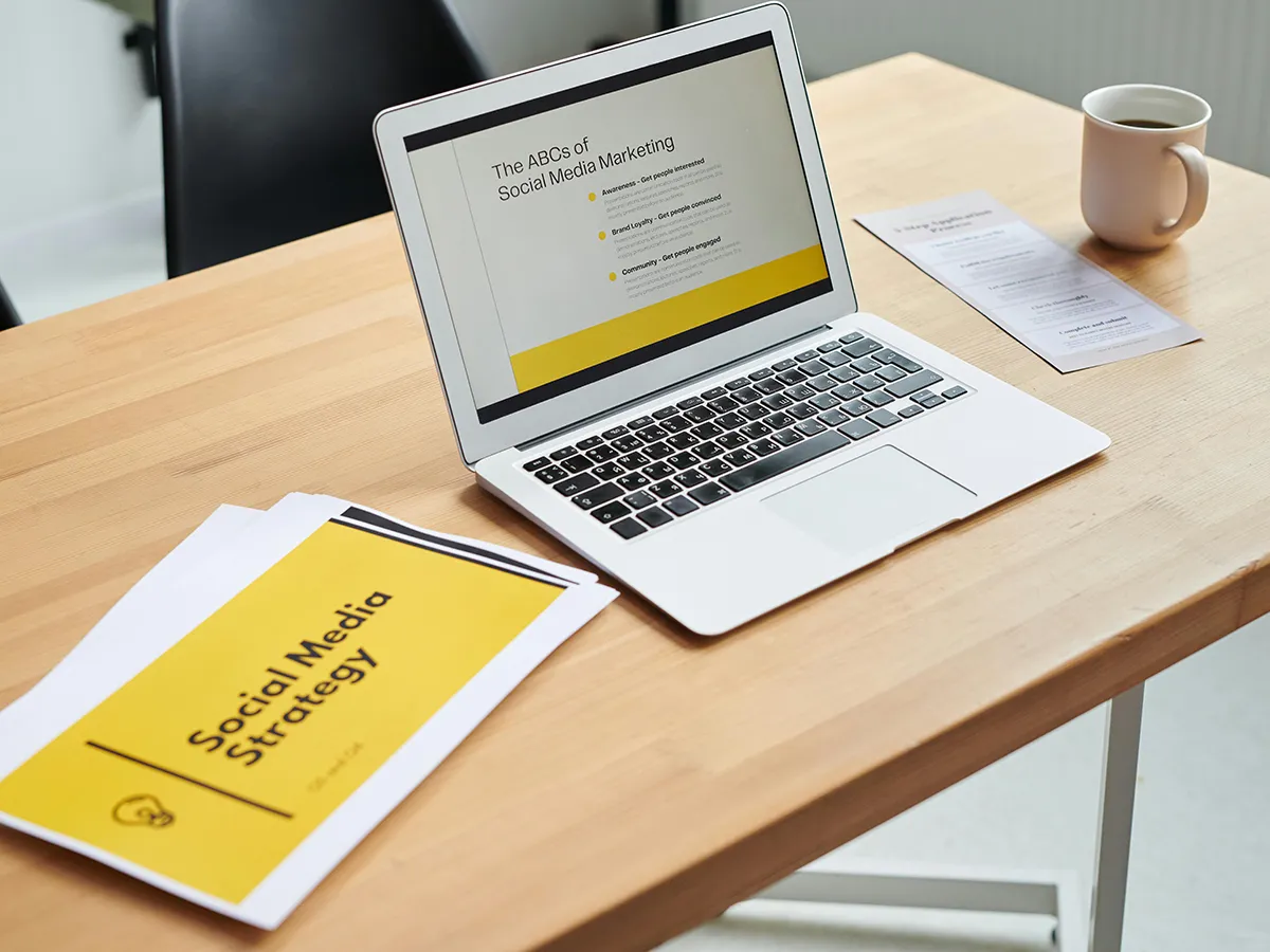 Laptop displaying a social media marketing presentation with printed social media strategy documents on the table.
