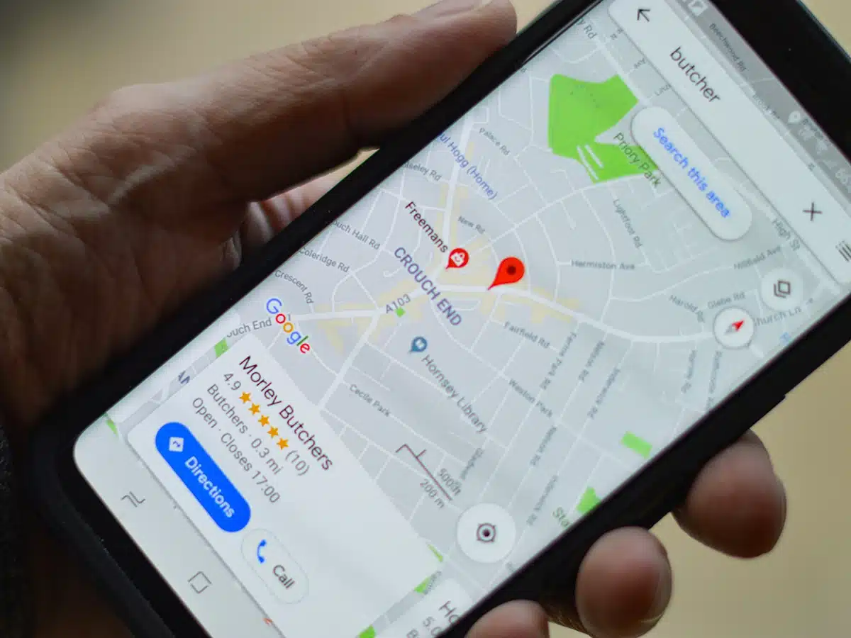 Hand holding smartphone showing Google Maps local search results for butcher with nearby business listings and map pins.